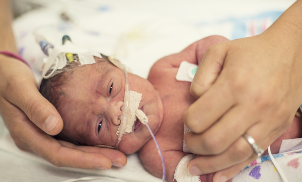 Mother holding her premature newborn baby as he is hooked up to an IV and health monitors while being treated in intensive care