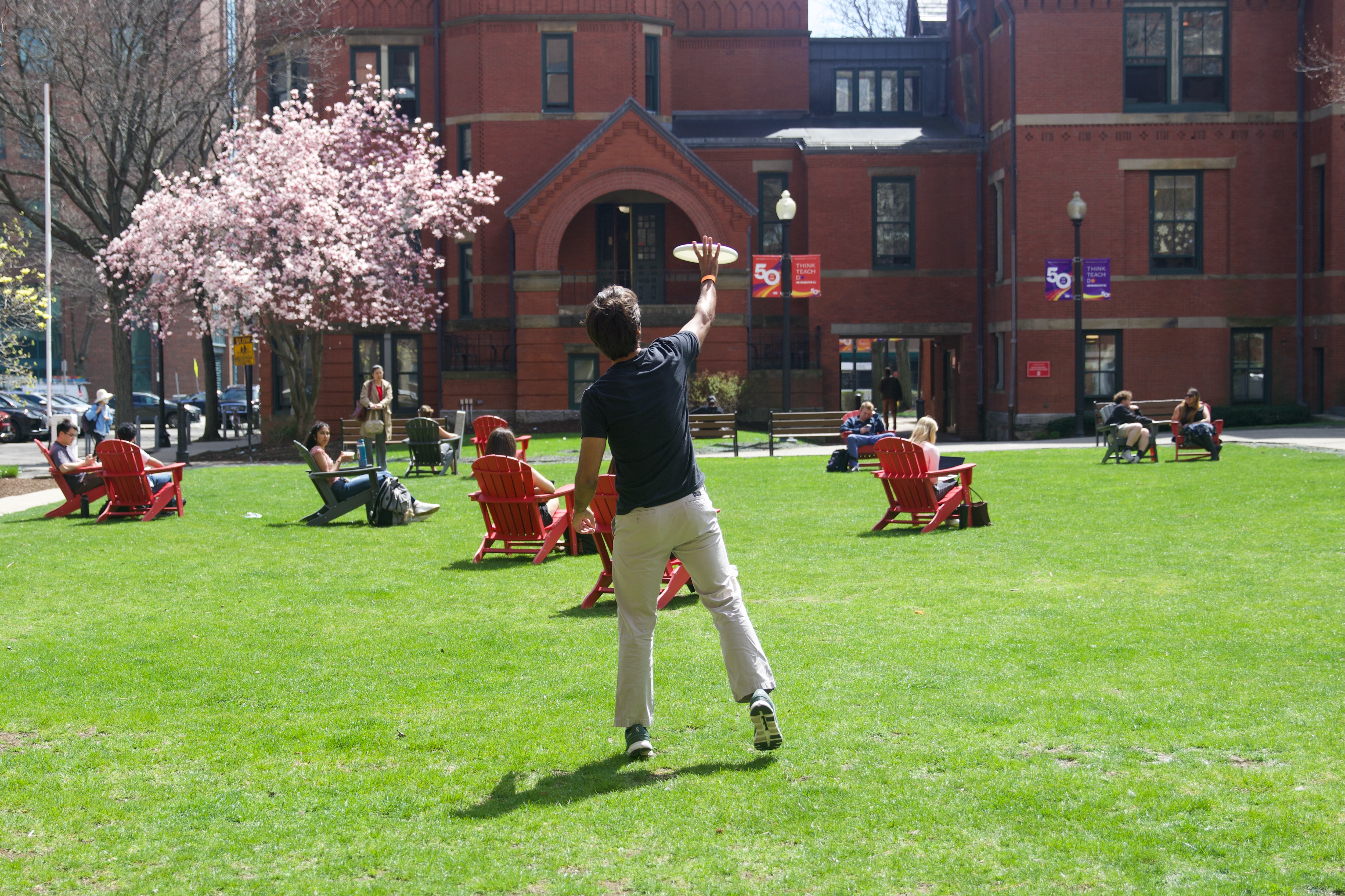 A student catches a frisbee while others relax in Adirondack chairs across Talbot Green on a sunny day. Photo: Megan Jones