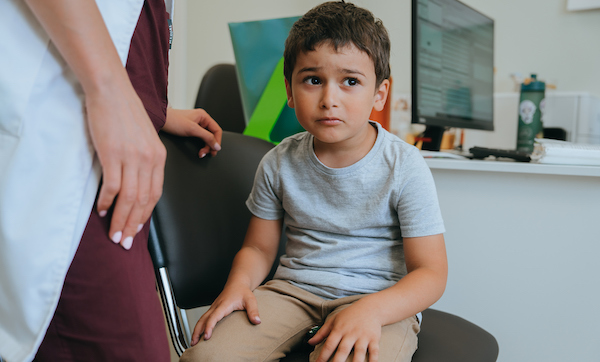 Sad frightened little boy sitting at medical office on chair looks aside with scared face expression. Caucasian toddler waiting for medical examining at hospital.