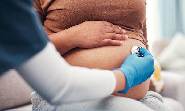 Closeup, pregnant and woman with healthcare checkup and stomach with wellness, appointment and results. Zoom, pregnancy and female with doctor, stethoscope and medical professional for consultation