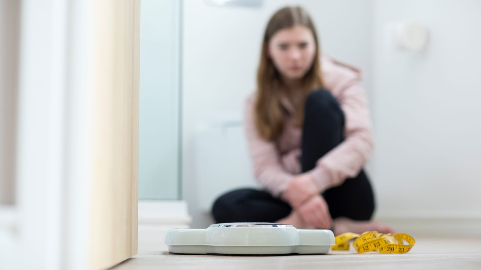 Young person sits on floor in front of scale and tape measure