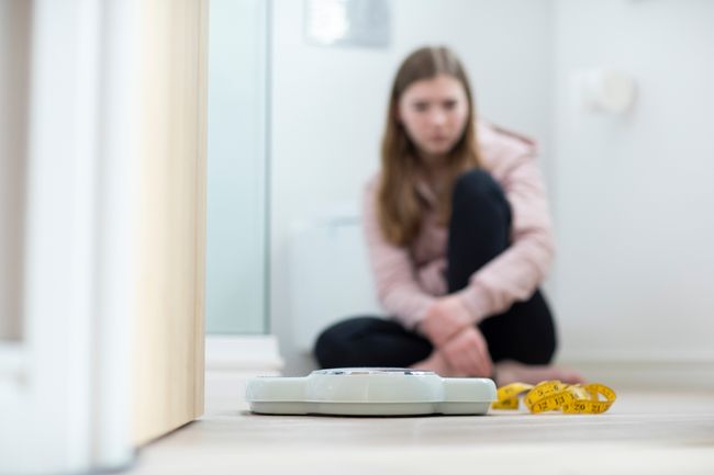 Young person sits on floor in front of scale and tape measure