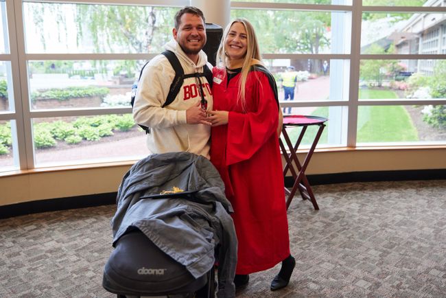 Photo of BUSSW graduate in red robe with guest and baby stroller
