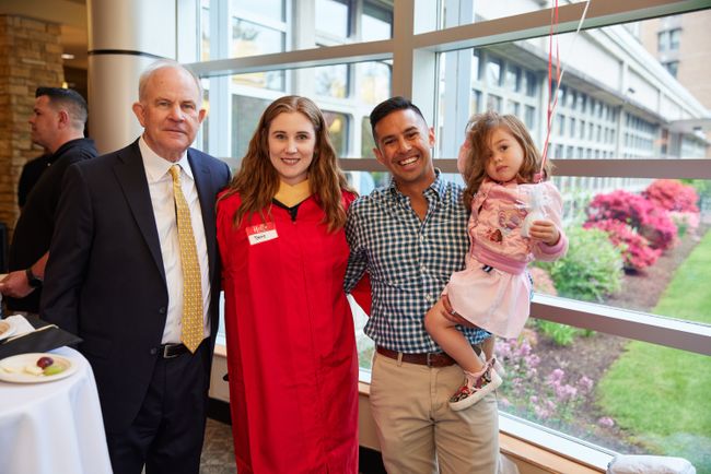 A BUSSW graduate and their guests pose for a photo in front of large windows