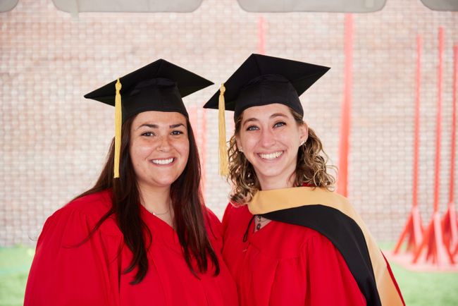 Two grads smile for a picture outdoors in the line-up tent