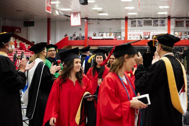 Students process into the arena in line; two lines of faculty clap for them on either side of the procession line