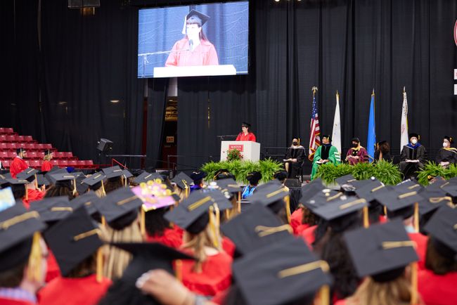 A student speaker is shown on the jumbotron as grads look on.