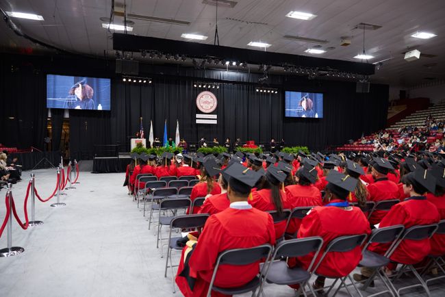 Rows of graduates are shown in front of Commencement Speaker Julia Mejia speaks from the podium