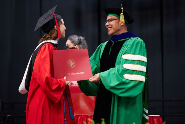 An MSW student receives their degree and greets Dean Delva onstage