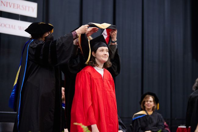 An MSW graduate is hooded on stage