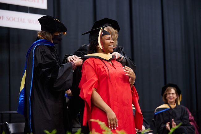 An MSW graduate is hooded on stage