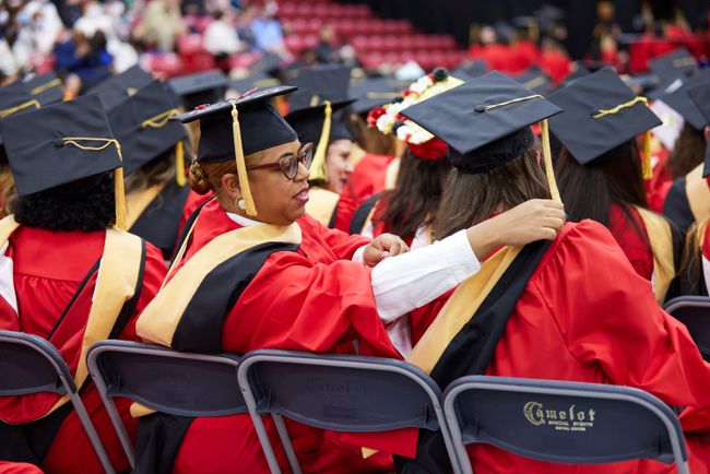 A grad helps another graduate with their hood