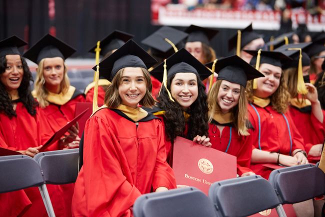 Grads smile for a photo from their seat with diplomas in hand