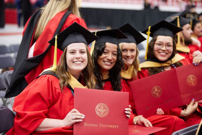 Grads smile for a photo from their seat with diplomas in hand