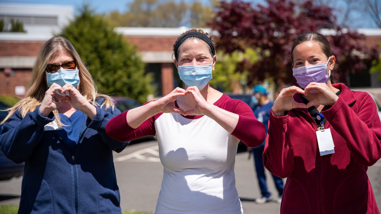 3 professionals wearing masks make a heart with their hands