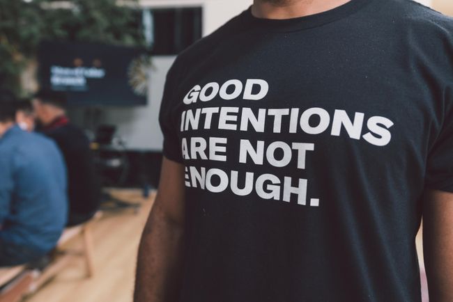 a black man wearing a t-shirt that says "Good Intentions are not enough"