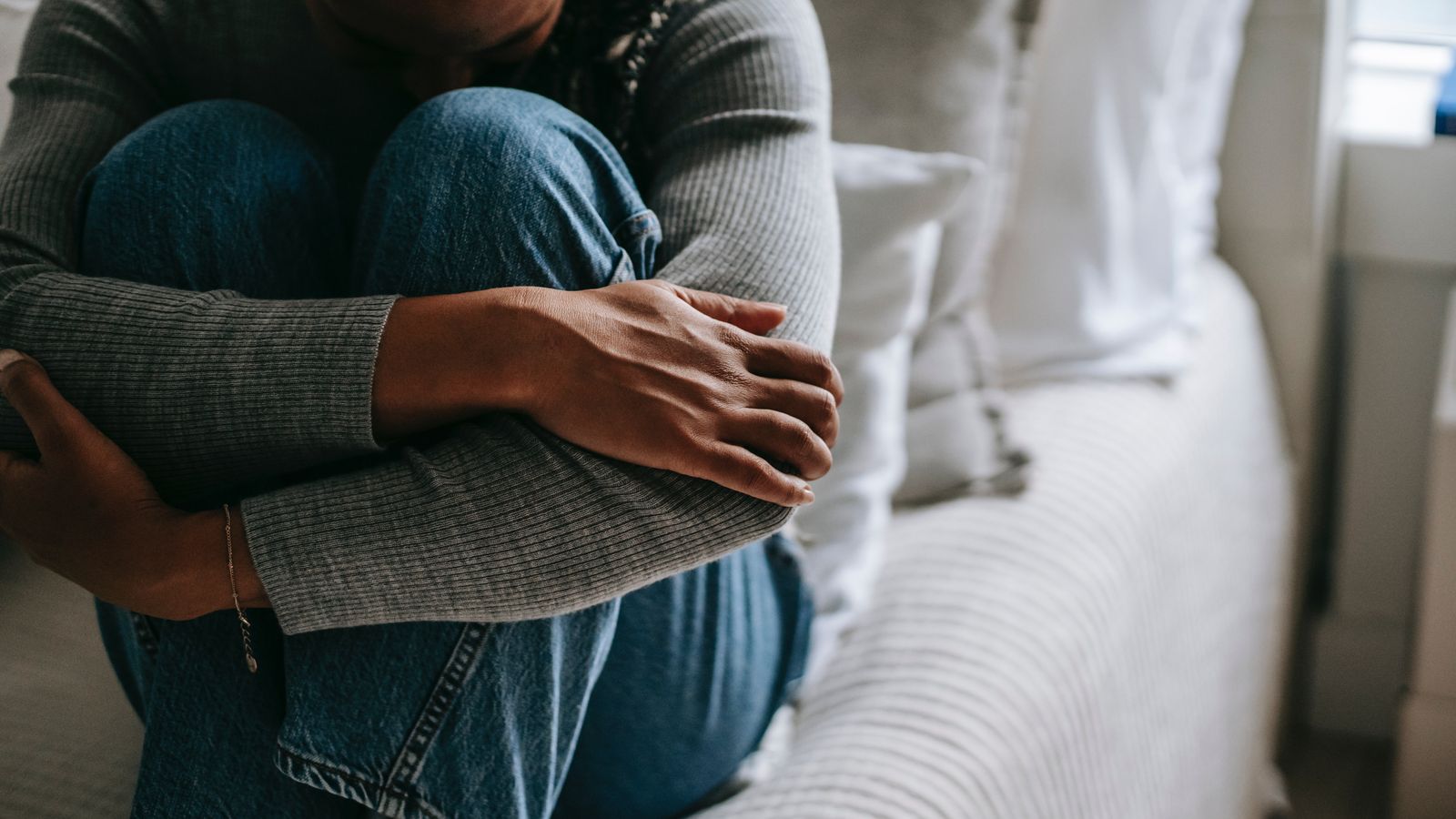 a woman hugging her knees on a bed.