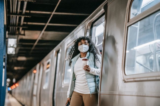woman holding coffee cup exits a subway carriage