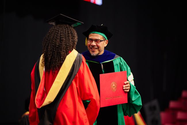 Graduating student receives diploma from Dean Delva on stage