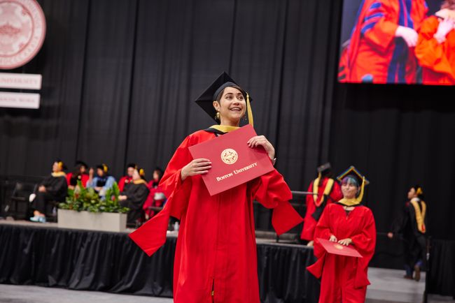 Smiling graduate walks back to seat with diploma