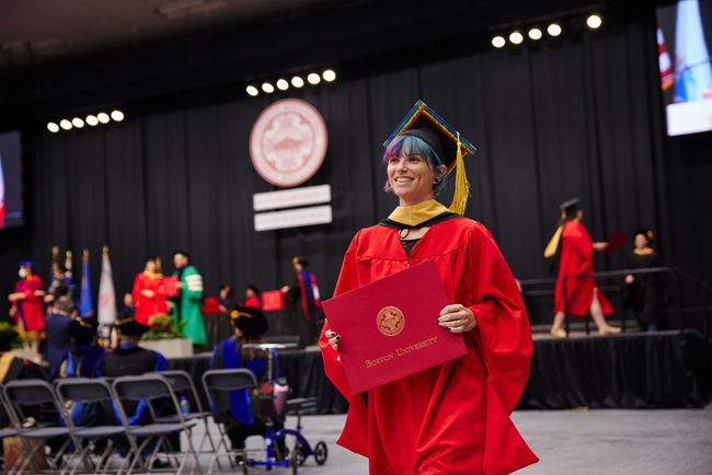 Smiling graduate walks back to seat with diploma