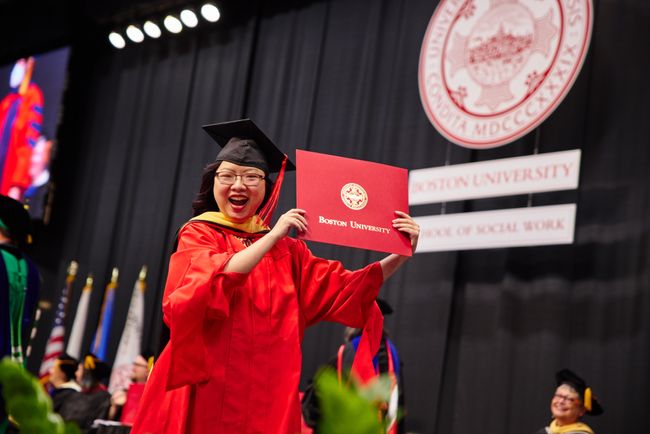 Smiling graduate walks back to seat with diploma
