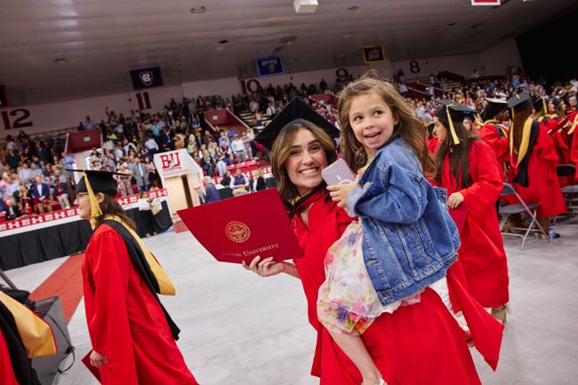 Smiling graduate holds child and diploma at post-ceremony reception