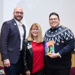 Photo of BU professors Carlos Rodriguez-Diaz and Luis Alvarez-Hernandez posing on stage with BUSSW Dean Barbara Jones and a copy of the See Me book