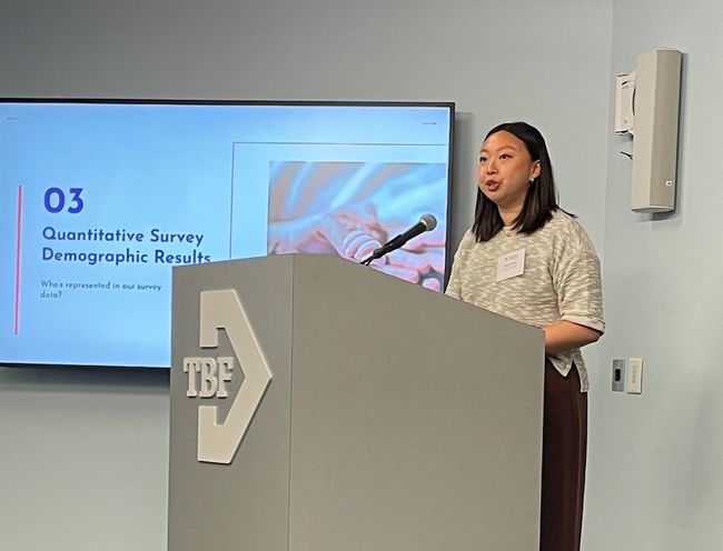 Zhang speaks at podium in front of screen with slide that says "03 Quantitative Survey Demographic Results"
