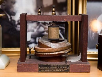 Model of original phone created by Alexander Graham Bell - A brown wood base with two pieces of wood on each side approximately six inches apart.. Wood piece above the round metal disks in center have wax pieces attached to them. Plaque on front says "Model of telephone"