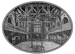 Interior of Hemenway gym at Harvard University. Image of two floors with open center space with ropes, long poles reaching from floor to ceiling, and benches on ground. Equipment would have been used for rehabilitation