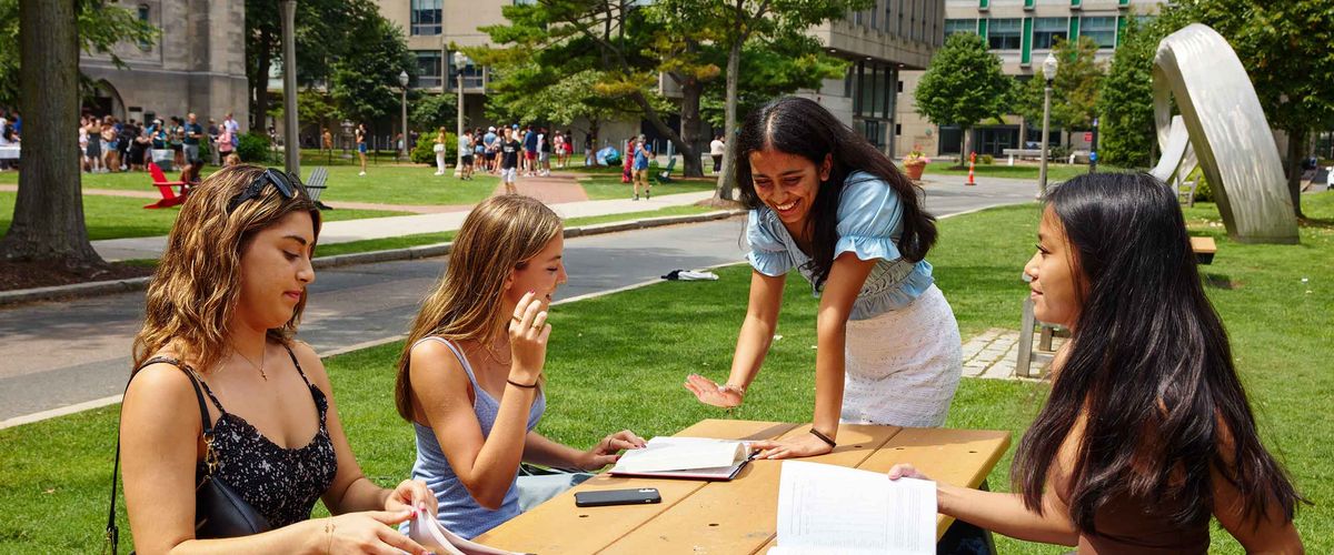 Four Boston University sit at a table on a sunny day.