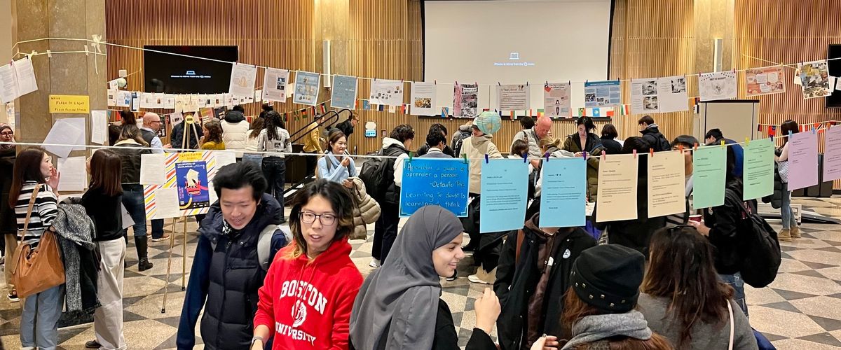 Students mingle in a large room with displays of writing in multiple languages hung around them.