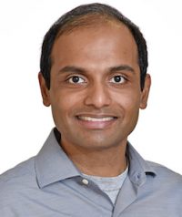 Portrait of Assistant Professor Vijaya Kolachalama wearing a blue-gray professional button-down shirt, photographed against a white background.
