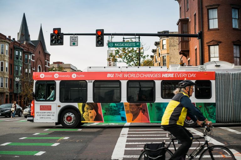A Boston University shuttle bus on a city street with a cyclist passing by.