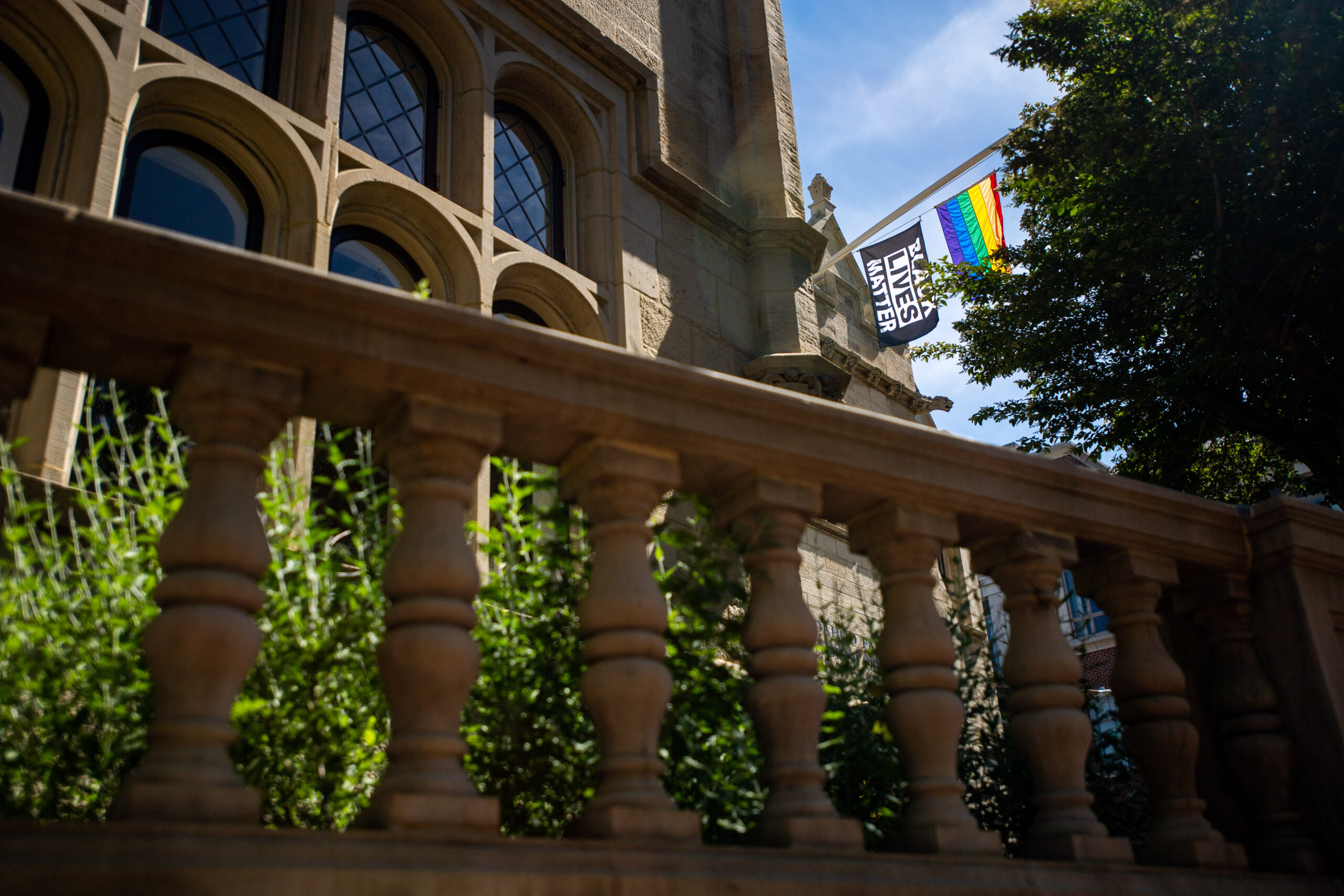 The side of a BU building showing stone balusters supporting the hand rail on top and the Black Lives Matter and pride flags attached to the building blowing in the wind on the top right corner of the photo.