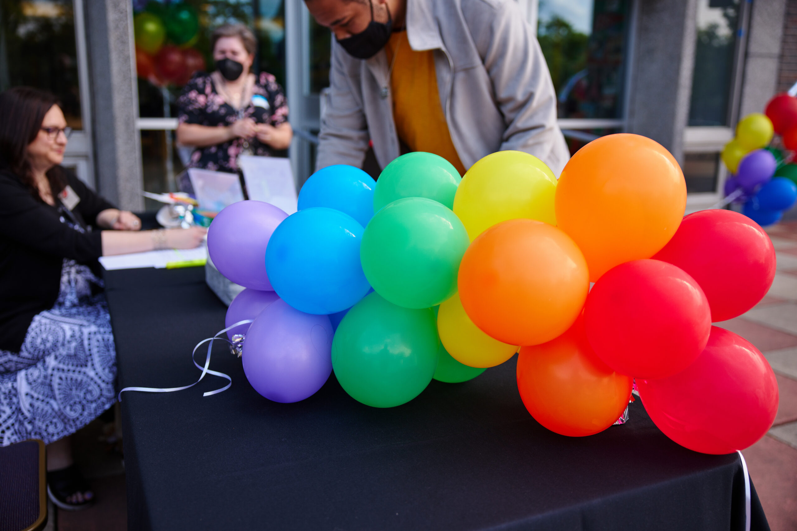 A mini rainbow balloon arch on a check in table at an event with people checking in in the background.