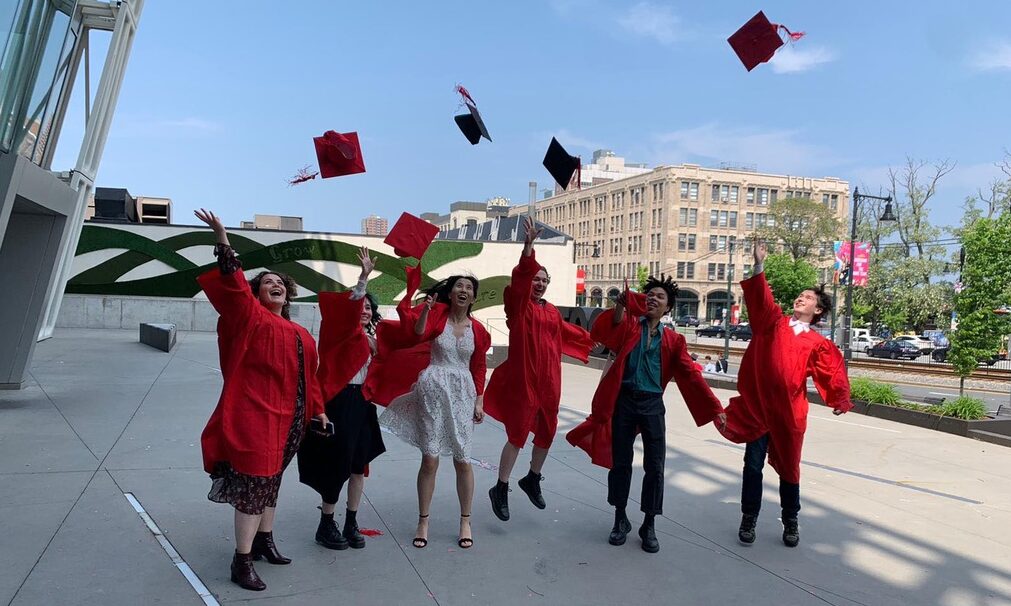 Translation students in graduate regalia throw their caps.
