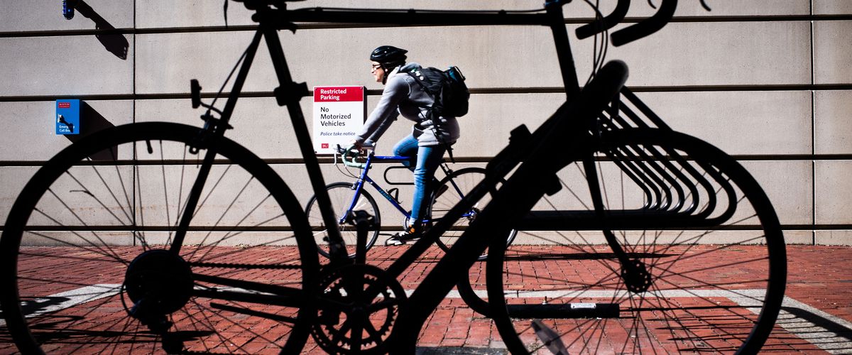 Person biking behind black silhouette of bike in rack