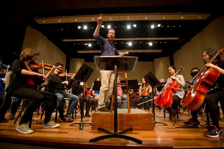 Conductor with student orchestra rehearsing