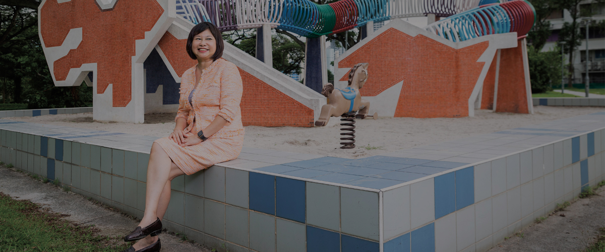 Ho Yin Fong sitting in a coral suit at a park smiling