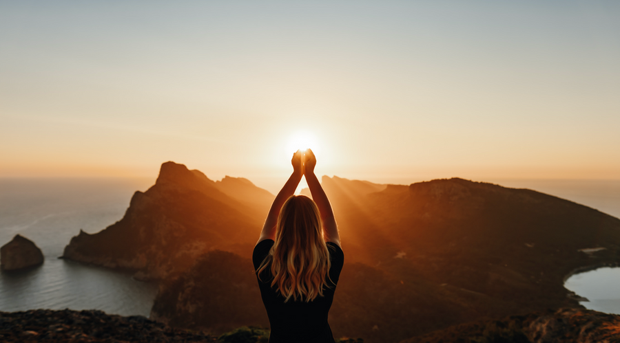 A person standing in front of a sunset, holding their hands up to the light.