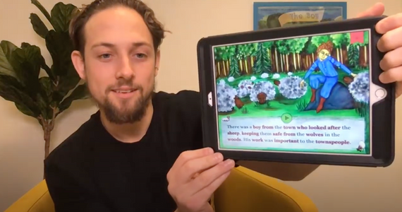 Conrad Baer (on the left) shows a page (on an iPad) from one of his Storybook Applications. The top 2/3 of the screen is an illustration with three lines of text below.