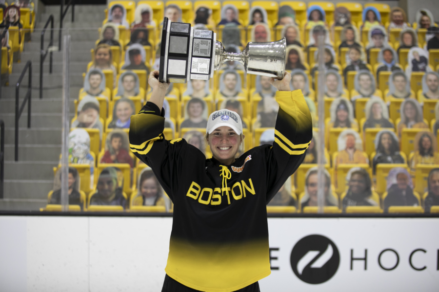 Women in black and yellow hockey jersey smiles holding a trophy above her head