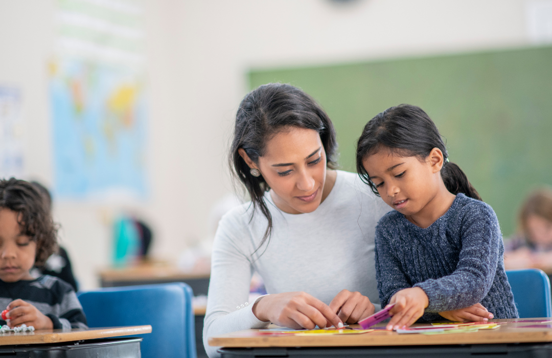 Young female teacher at desk helping student