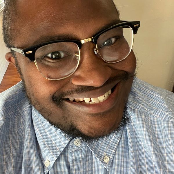 Photo of a Black man in glasses and a blue button-down Oxford shirt.