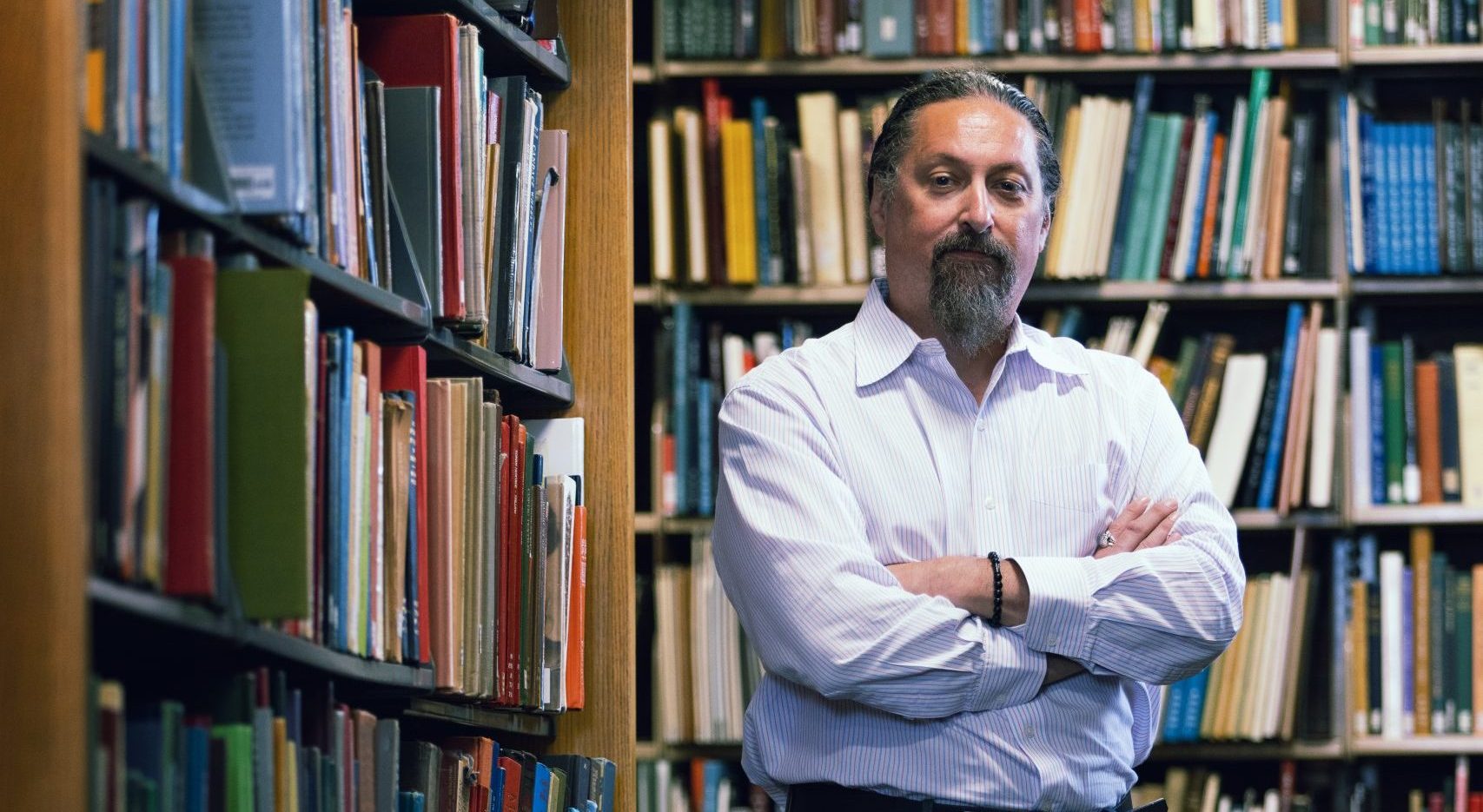 Hank Fien stand arms crossed in front of bookshelves