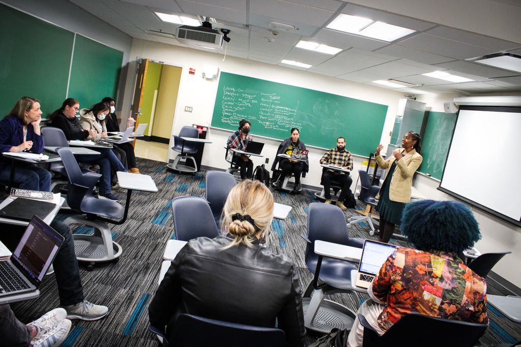 Shows a professor teaching a class of graduate students