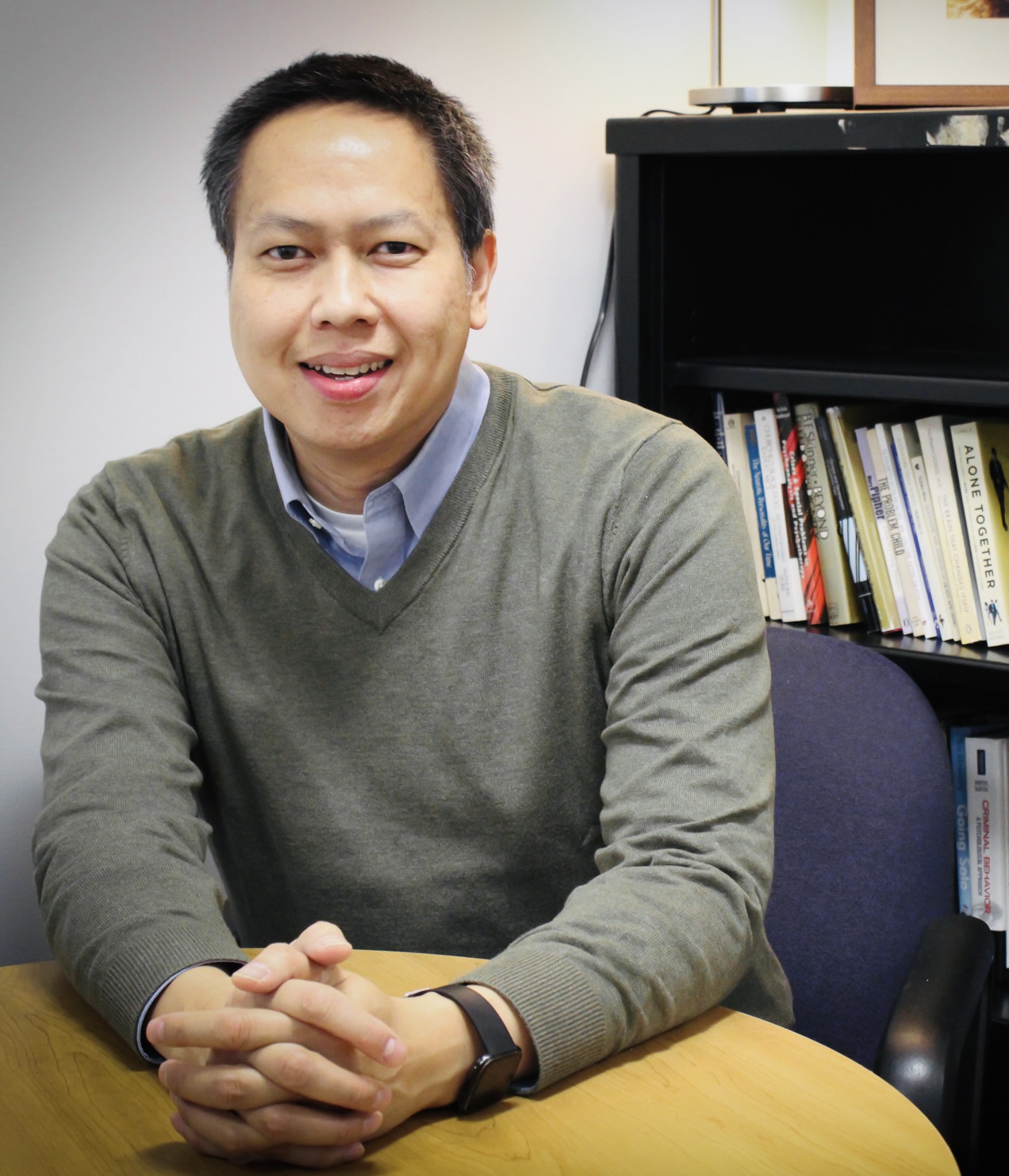Photo of Bobby Hiep Bui sitting in front of bookshelf with hands clasped together