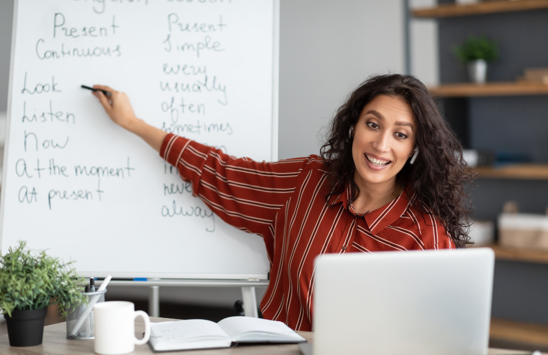 teacher pointing to while board speaking to computer